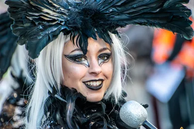 Mujer con peluca blanca y tocado de plumas negras, cantando ante un micrófono.