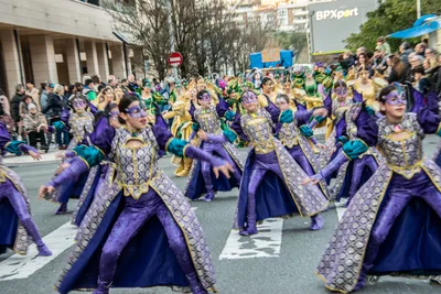 Comparsa morada y dorada bailando a la vez en mitad de la calzada.