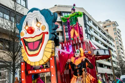 Carroza con una cabeza de payaso gigante y dos zancudos a su lado.