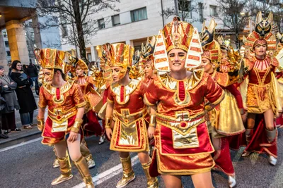 Comparsa egipcia de rojo y dorado avanzando por la calzada en formación.