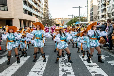 Comparsa de mosqueteros con sombreros naranjas cruzando un paso de cebra.