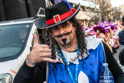 Hombre disfrazado de mosquetero, con bigote pintado y sombrero rojo y negro.