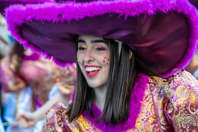 Joven con un sombrero morado ribeteado de plumón, riendo.