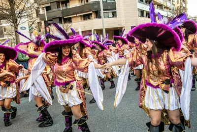 Comparsa de mosqueteros morados y dorados bailando en mitad de la avenida.