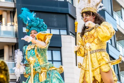 Dos figuras de carroza: una de turquesa con plumas y otra de dorado con un sol bordado.