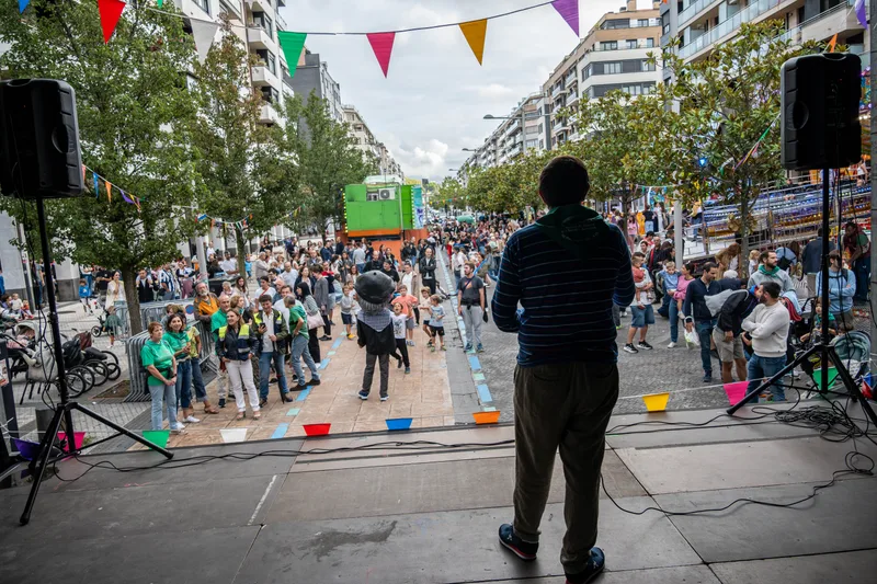 Desde el escenario, de espaldas, un hombre mira la avenida de Barcelona llena de gente bajo los banderines de colores.