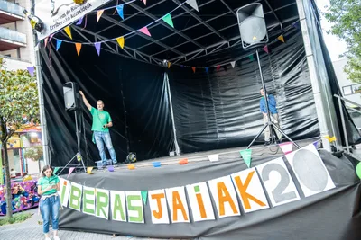 El escenario de la avenida de día, con un hombre de camiseta verde arriba y la pancarta «Riberas Jaiak 20» de letras sueltas abajo.
