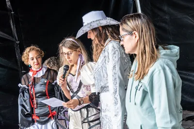 Las pregoneras de Erriberatarrak, disfrazadas con sombrero vaquero de lentejuelas, vestido de época y traje negro de volantes, leen el pregón con un papel y un micrófono.