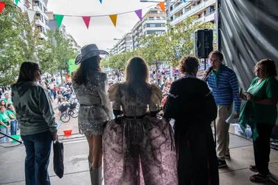 Desde detrás, las pregoneras y el presentador en el borde del escenario, con la avenida llena delante.