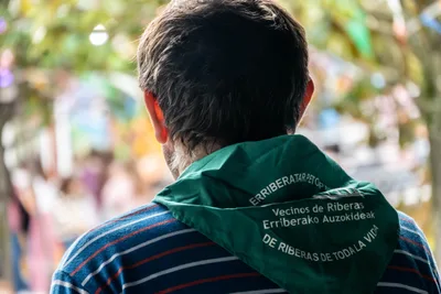 La espalda de un hombre con el pañuelo de las fiestas: «Vecinos de Riberas · Erriberako Auzokideak · De Riberas de toda la vida».