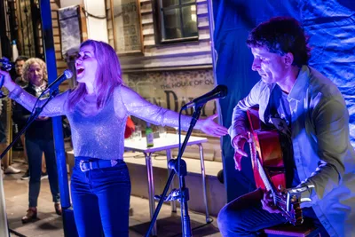 Radio Rebelde en la terraza: la cantante con los brazos abiertos y el guitarrista sentado, con público detrás.