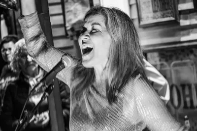En blanco y negro, la cantante de Radio Rebelde con el brazo en alto y la boca abierta en mitad de una canción.