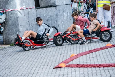 Tres chavales recostados en karts rojos de pedales recorren un circuito marcado con conos.