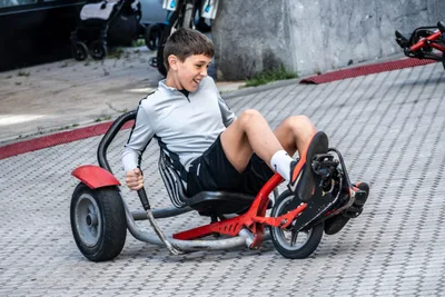 Un chaval sonríe tumbado en un kart rojo de pedales, tomando una curva.