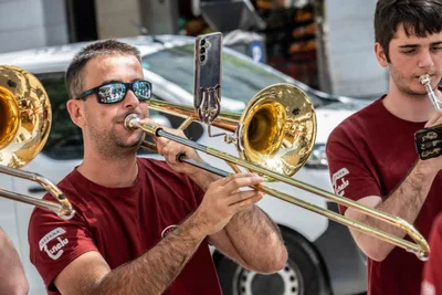 Un trombonista de la txaranga con gafas de sol y camiseta granate toca junto a un compañero.