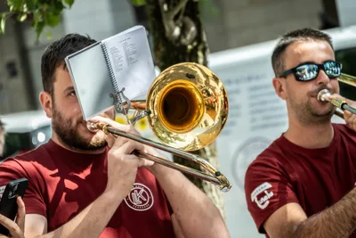 Un trombonista lee la partitura de un atril de bolsillo mientras otro toca a su lado.