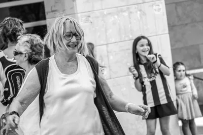 En blanco y negro, una mujer con gafas baila riendo; detrás, una niña con la camiseta de la Real.