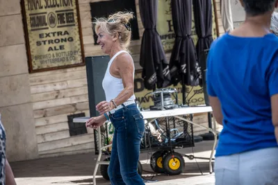 Una mujer rubia con camiseta blanca de tirantes se ríe mientras baila.