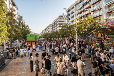 La avenida de Barcelona llena de gente a última hora de la tarde, con las atracciones de feria a la derecha.