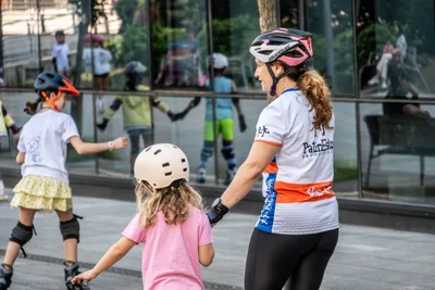 Una monitora de Patin Eskola lleva de la mano a una niña con casco; otras niñas patinan alrededor.