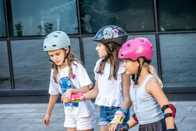 Tres niñas con casco y protecciones; una agarra del brazo a la otra para no caerse.