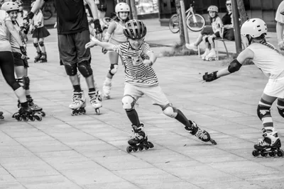 En blanco y negro, un niño con camiseta de rayas patina con los brazos abiertos entre otros patinadores.