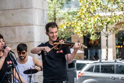 El violinista de Riber Rockers sonríe tocando un violín eléctrico, con la batería detrás.