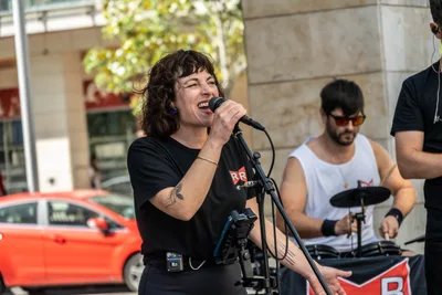 Una de las cantantes se ríe con el micrófono en la mano, con el batería al lado.