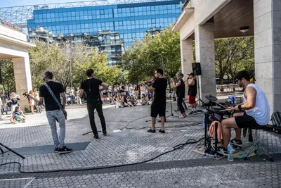 Desde detrás de la batería, el grupo toca en la plaza y el público escucha al fondo, al sol.