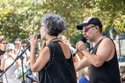Dos cantantes, ella de pelo canoso y él con gorra, cantan de cara al público que graba con el móvil.