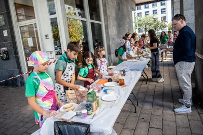 Niños con delantal preparan sus pintxos en la mesa larga; una lleva un gorro con los colores del arcoíris.