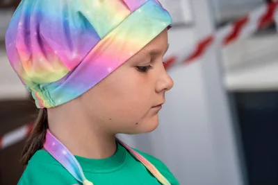 Una niña con un pañuelo de colores del arcoíris en la cabeza, de perfil, atenta a su plato.