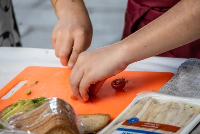 Unas manos cortan un tomate cherry sobre una tabla naranja, junto a un paquete de pan de molde.