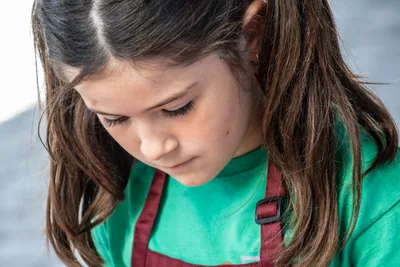 Una niña con camiseta verde y delantal granate, concentrada en lo que prepara.