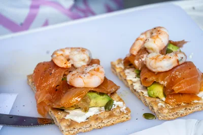 Dos tostas de salmón ahumado con aguacate y gambas, sobre una bandeja blanca.