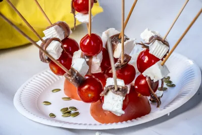 Brochetas de tomate cherry, queso fresco y anchoa clavadas en medio tomate, con pipas de calabaza alrededor.