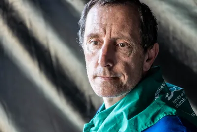 Un hombre de la comisión, con pañuelo verde, mira serio a cámara delante de la lona negra del escenario.