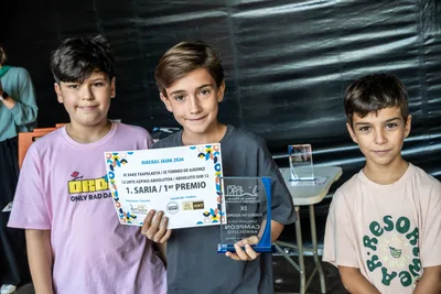 Tres chavales con sus diplomas y trofeos de cristal del torneo de ajedrez.