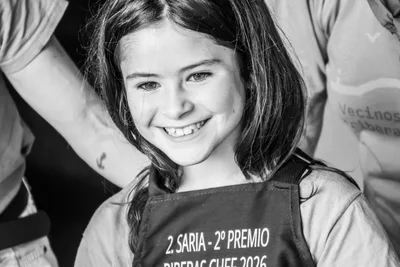 En blanco y negro, una niña sonríe con el delantal del segundo premio del Riberas Chef.