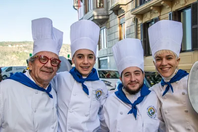 Cuatro cocineros de la tamborrada posan juntos en la calle, con chaquetilla blanca, gorro alto y pañuelo azul al cuello.