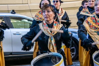 Mujeres con mantón de flores y falda amarilla tocan el tambor en plena calle.