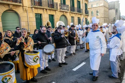La compañía entera ocupando la calzada: mantones y barriles delante, la banda de metales al fondo.
