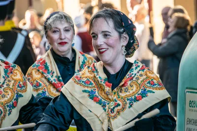 Dos mujeres con mantón de flores bordado y baqueta en la mano, riendo entre la formación.