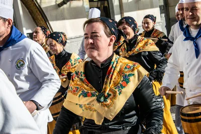 Una mujer con pañuelo a la cabeza y mantón de flores toca el barril entre los cocineros.
