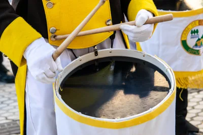 Detalle de dos manos con guante blanco tocando el tambor con las baquetas.