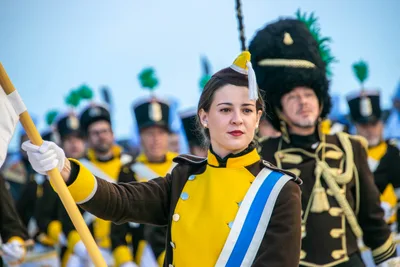 Una cantinera con la bandera y la banda azul y blanca; detrás, el tambor mayor con su gorro de piel.