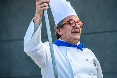 Un cocinero con gafas rojas levanta la pala de cocina sobre la cabeza.