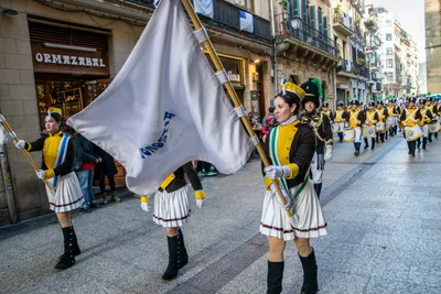 Dos cantineras hacen ondear las banderas en una calle estrecha, con la compañía formada detrás.
