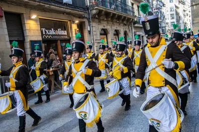 Los gastadores marchan por una calle de la Parte Vieja, con los bares a un lado y gente mirando.