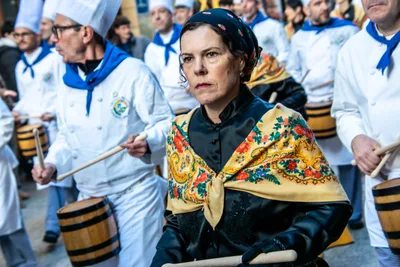 Una mujer con pañuelo a la cabeza y mantón de flores toca entre dos cocineros.